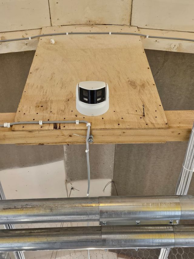 Dual-lens CCTV camera fixed to a timber mount in a poultry house roof